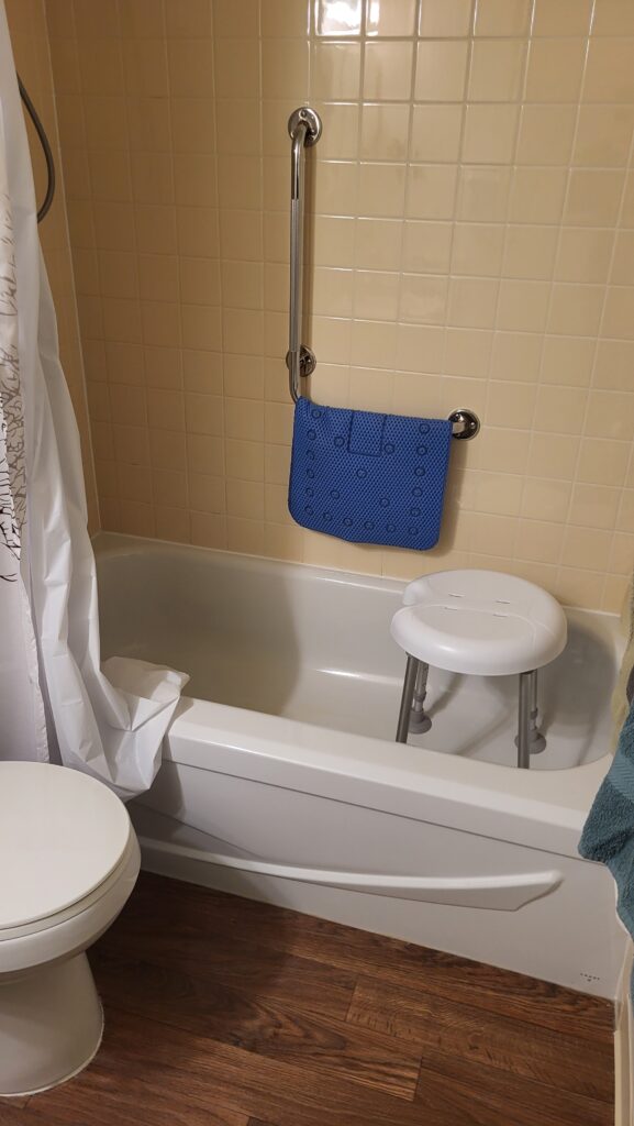 Bathtub with shower stool, vertical grab bar, and blue bath mat