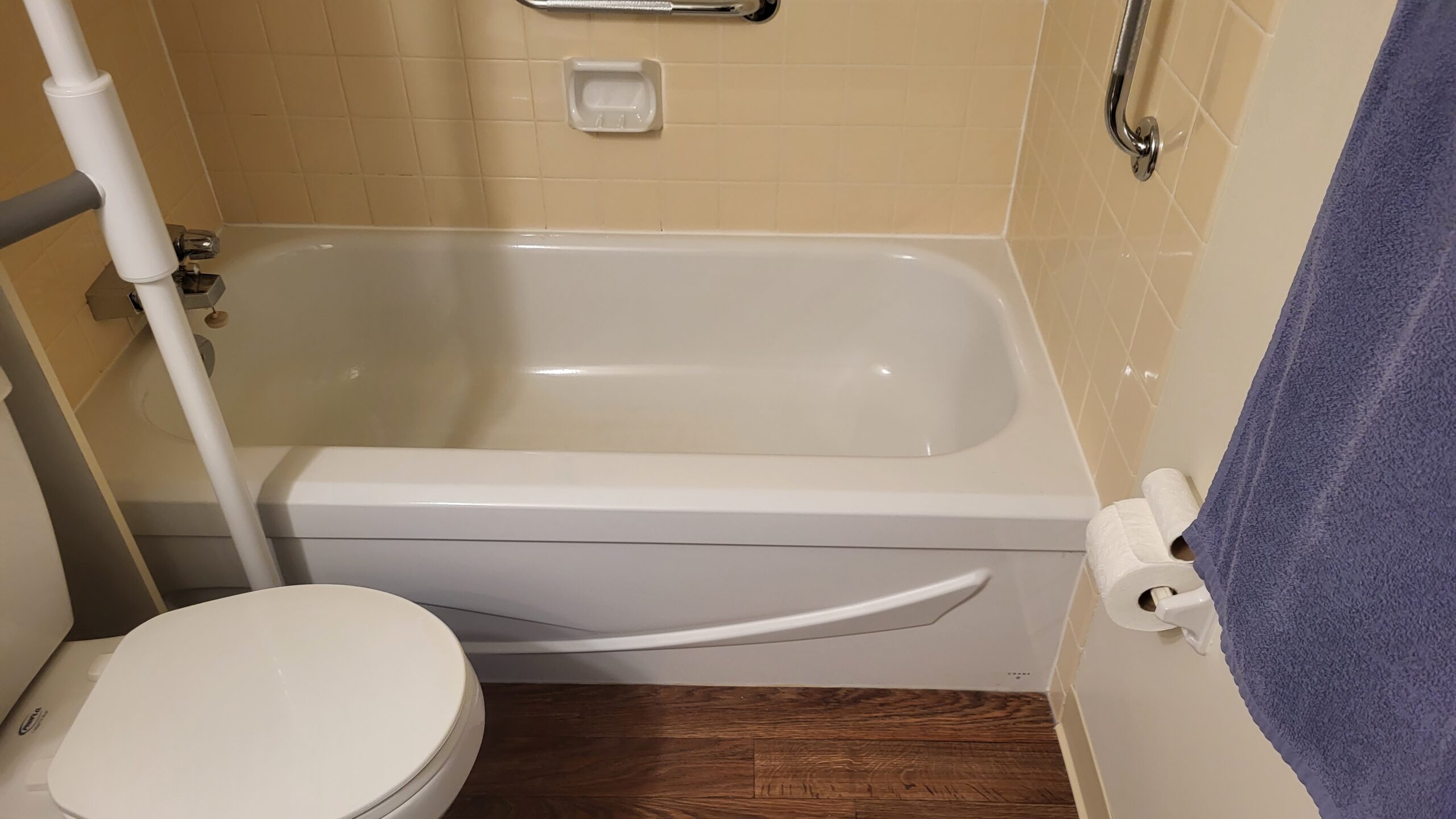 Bathroom with white bathtub, beige tile walls, and support grab bars