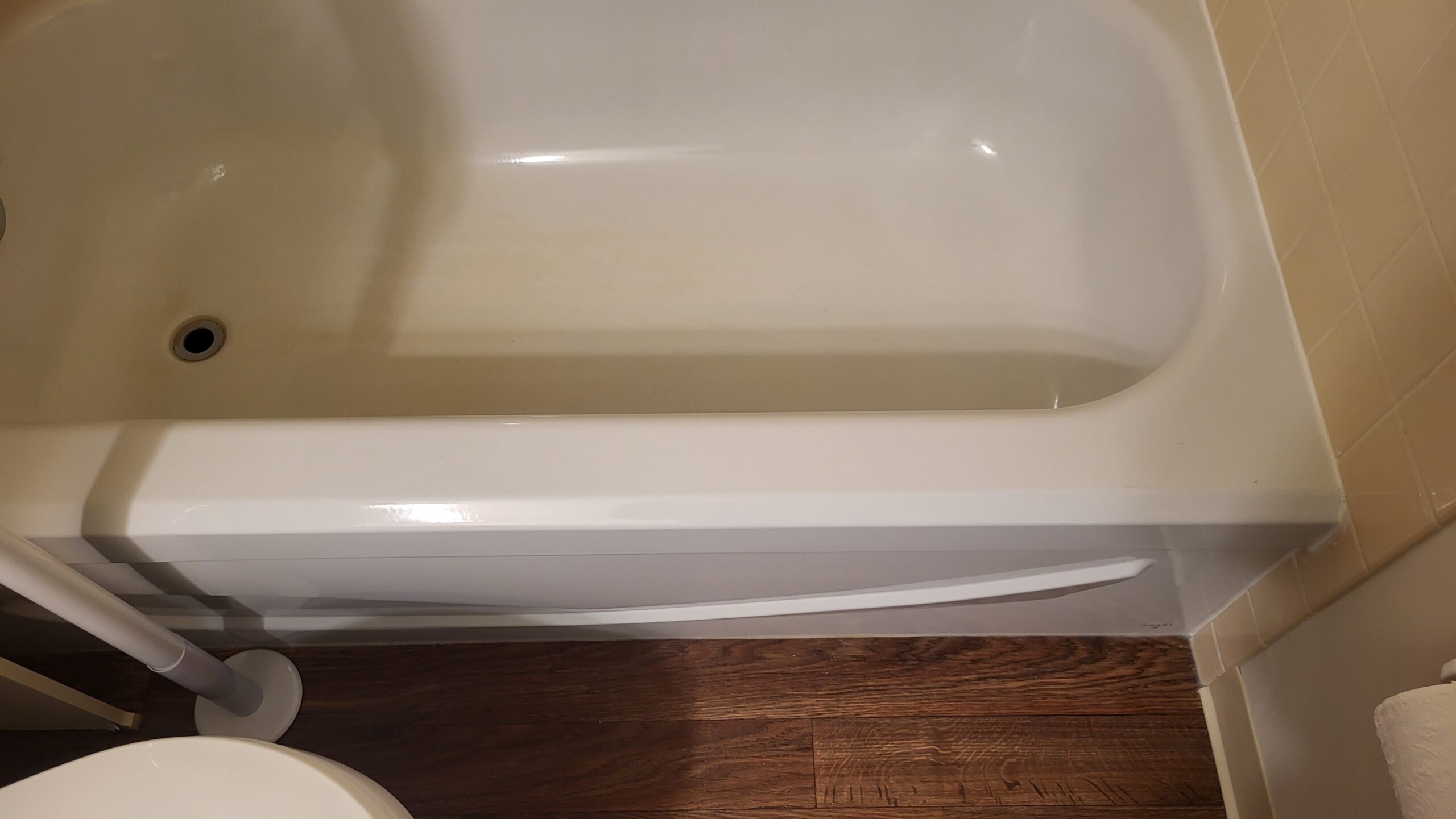 White bathtub interior with beige tile wall and dark vinyl flooring
