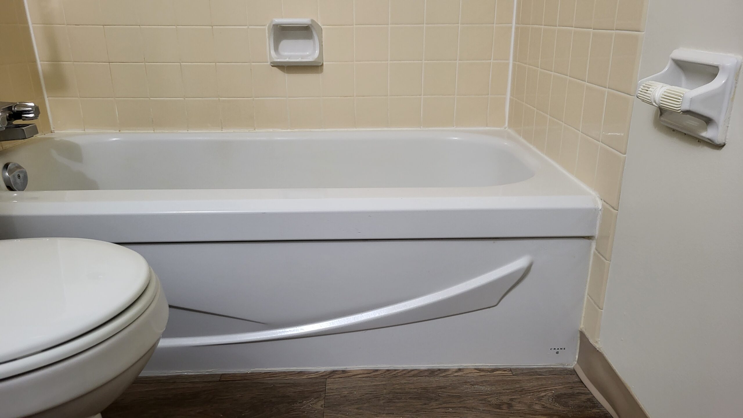 Standard white bathtub with tiled walls and no access panel, viewed from a side angle in a small bathroom