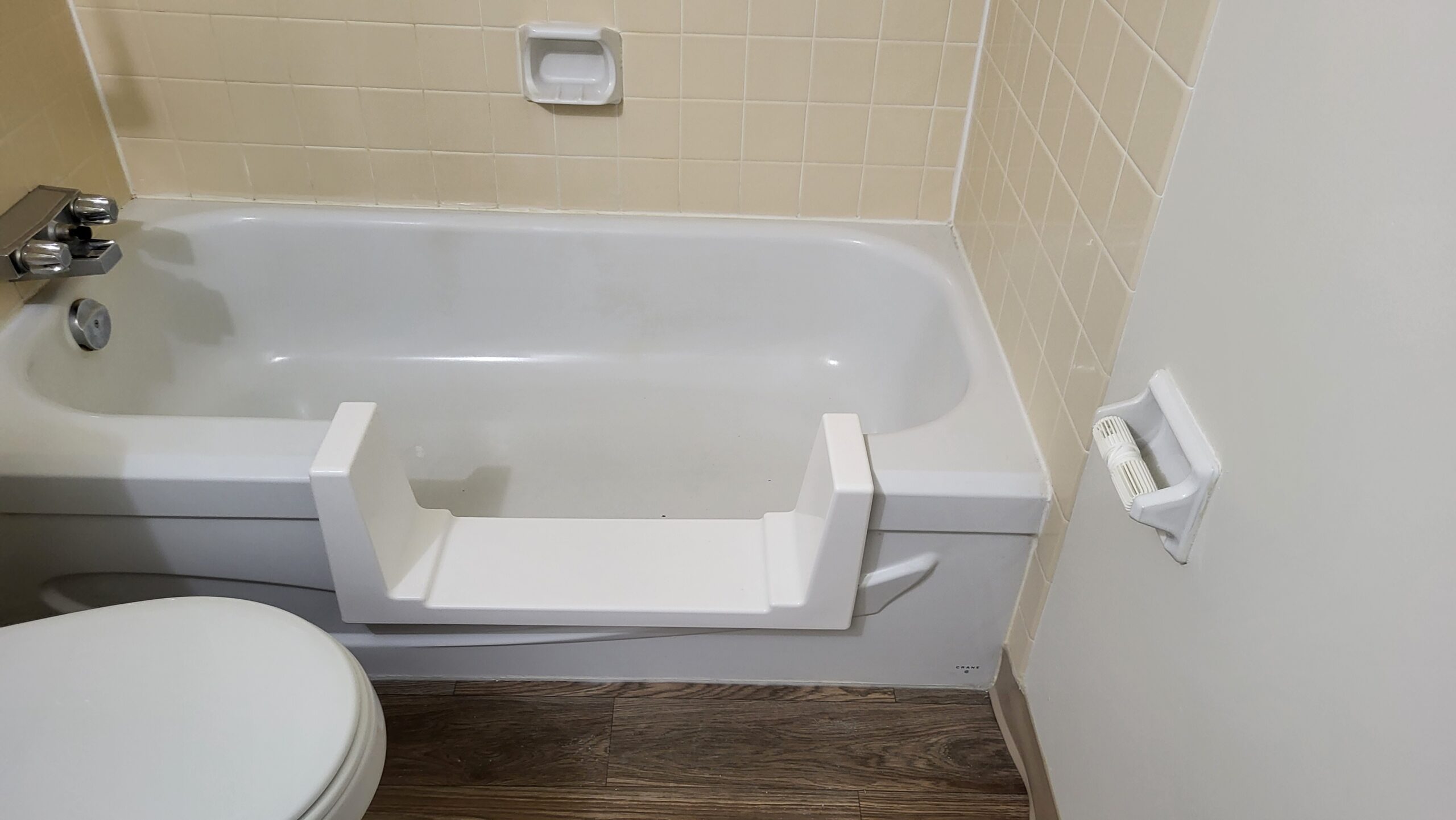 Bathtub modified with a cut-out step for easier entry, surrounded by beige tile and wood-look flooring