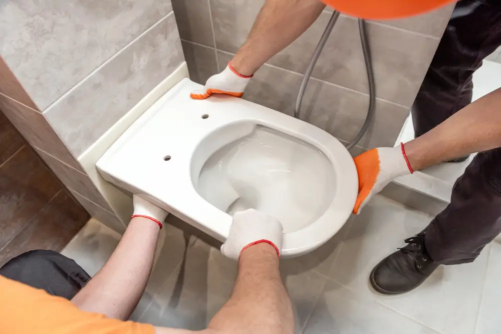 Workers installing a wall-mounted toilet in a tiled bathroom