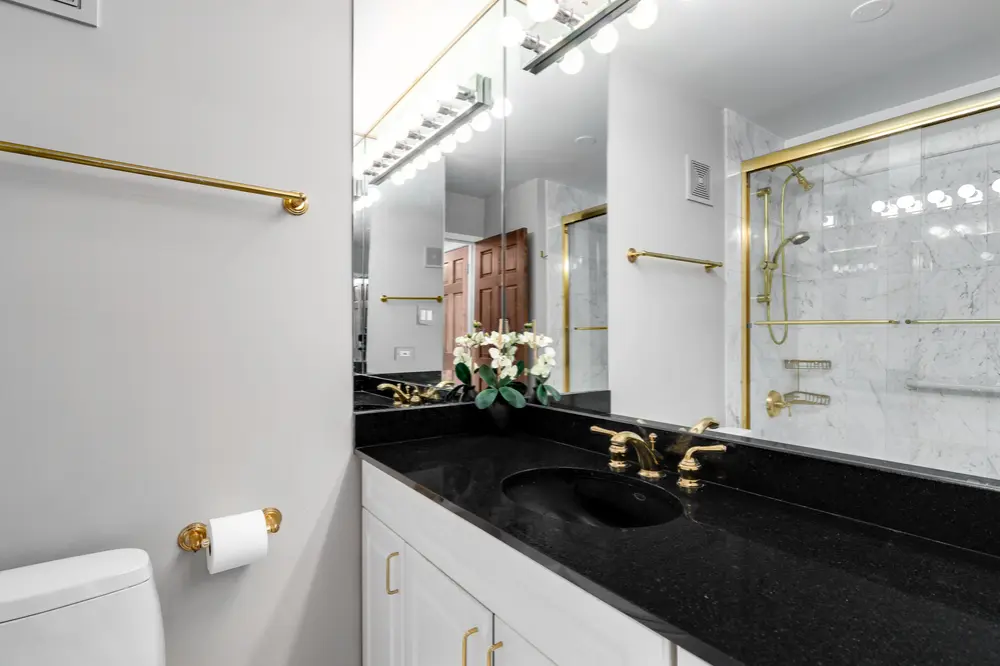 Luxury bathroom with black granite countertop, gold fixtures, and glass shower enclosure
