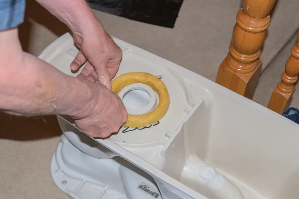 Hands installing a wax ring seal on the base of a toilet