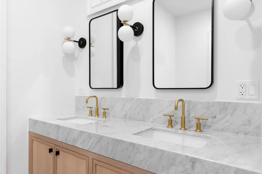 Modern double vanity with marble countertop, gold fixtures, and black-framed mirrors