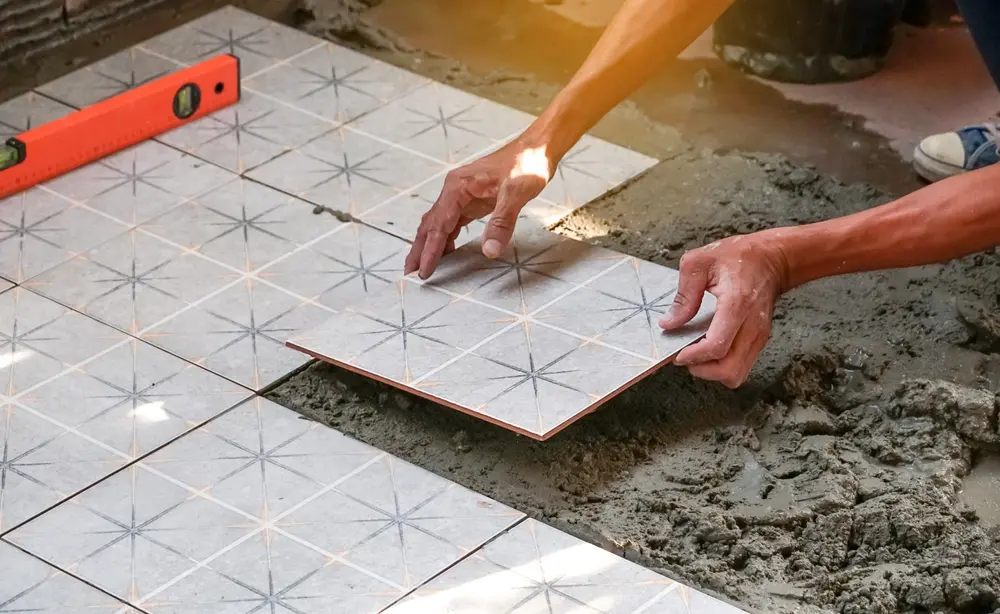Hands placing patterned ceramic tile on wet mortar during floor installation