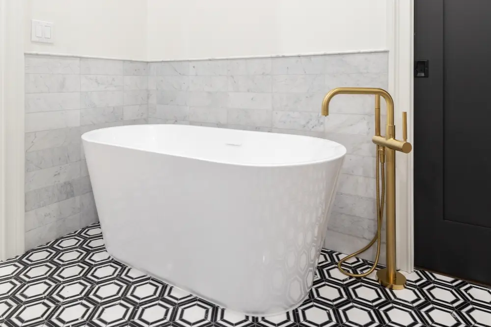 Modern freestanding white bathtub with gold floor-mounted faucet in a stylish bathroom
