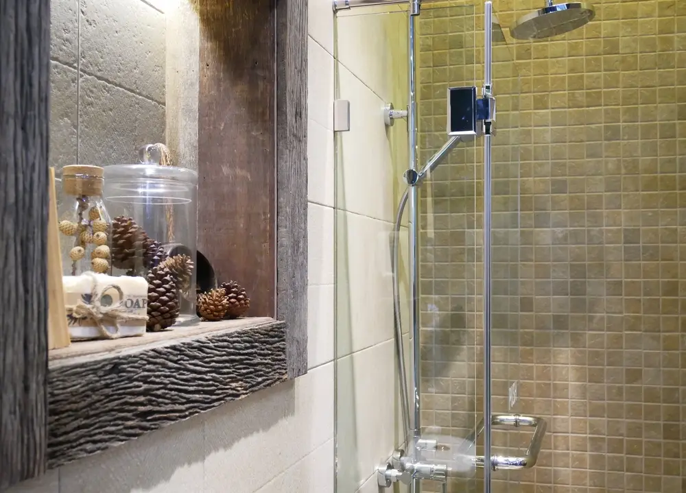 Rustic bathroom shower with glass door and pinecone decor on wooden shelf