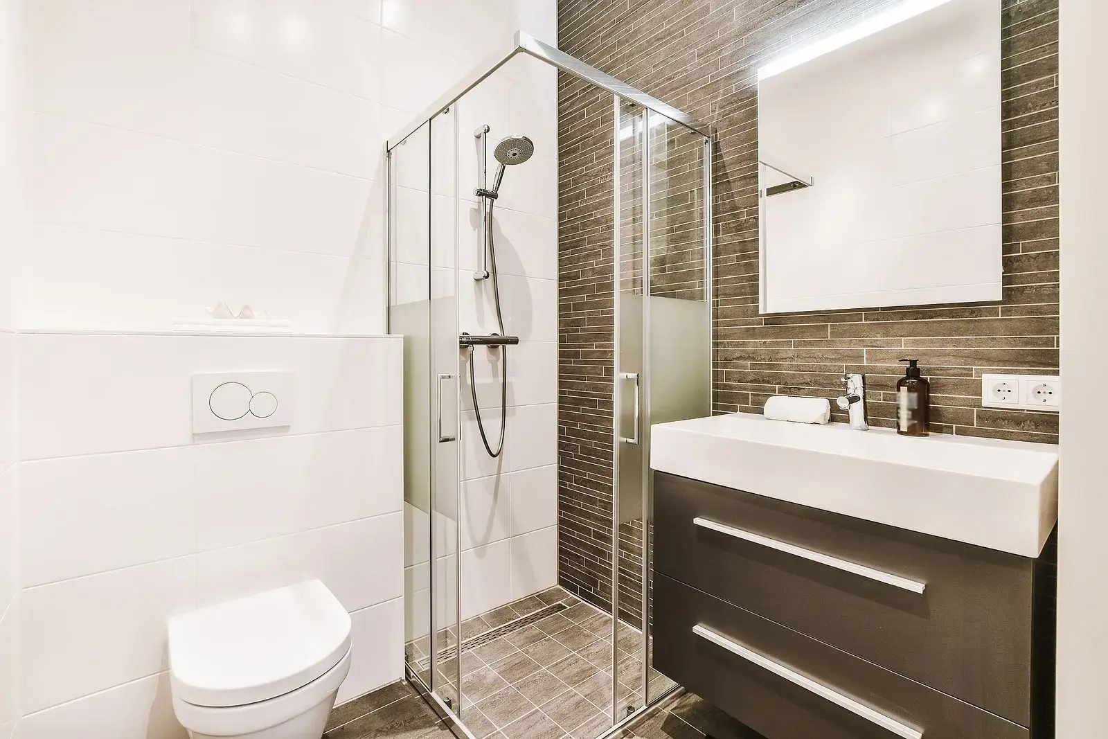 Modern small bathroom with glass shower enclosure, wall-mounted toilet, and dark vanity
