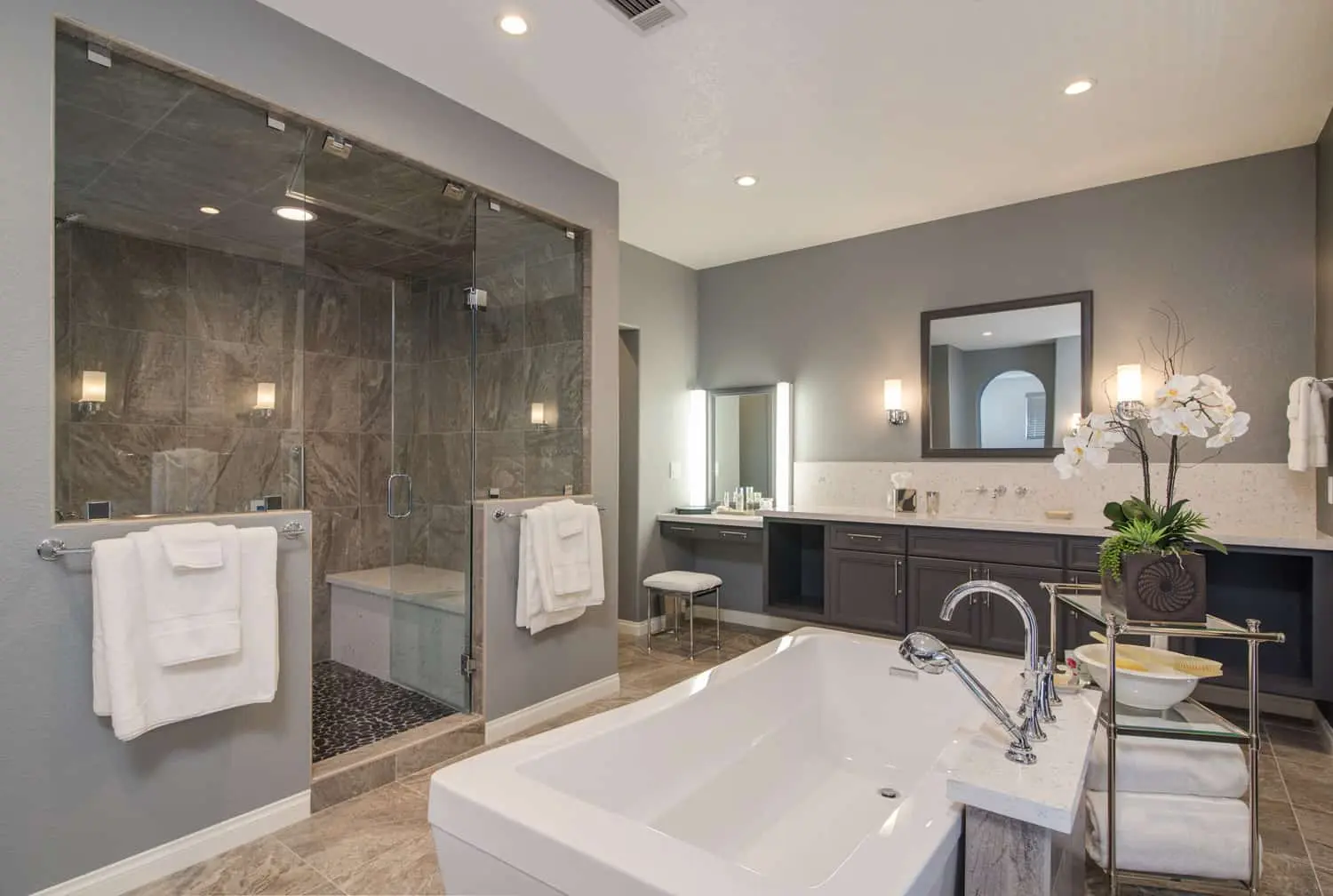 Luxury bathroom with glass shower, soaking tub, and dark double vanity