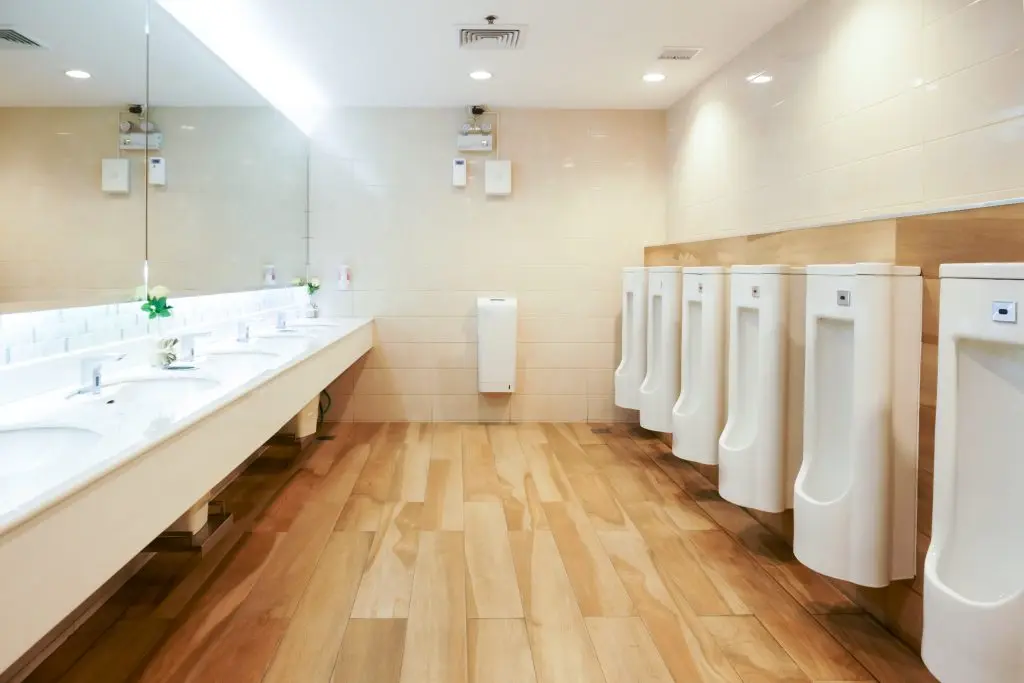 Modern men's public restroom with wall-mounted urinals and long countertop sinks.