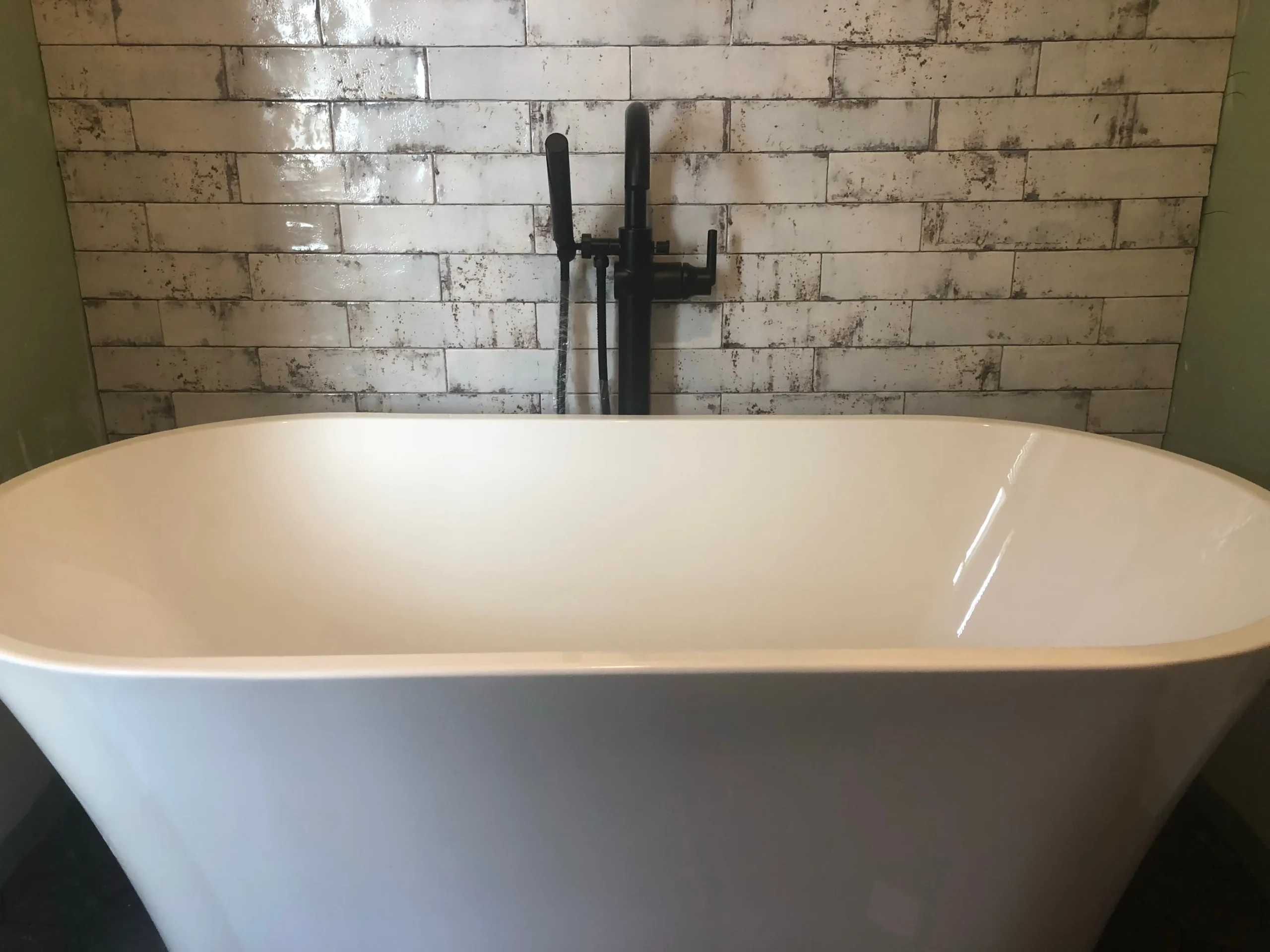 Freestanding white bathtub with rustic tile backsplash and matte black faucet