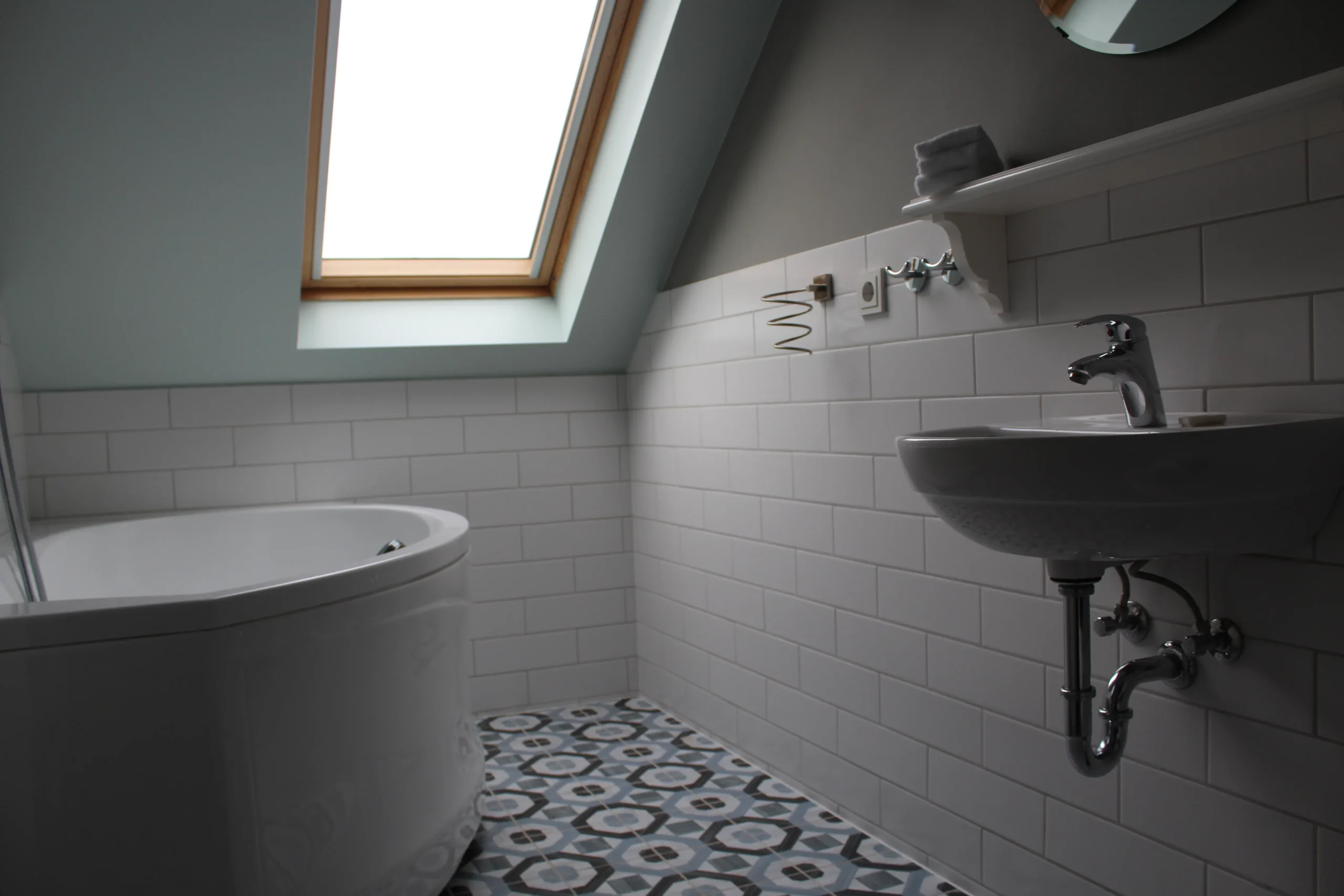Compact attic bathroom with skylight, bathtub, and patterned floor tiles