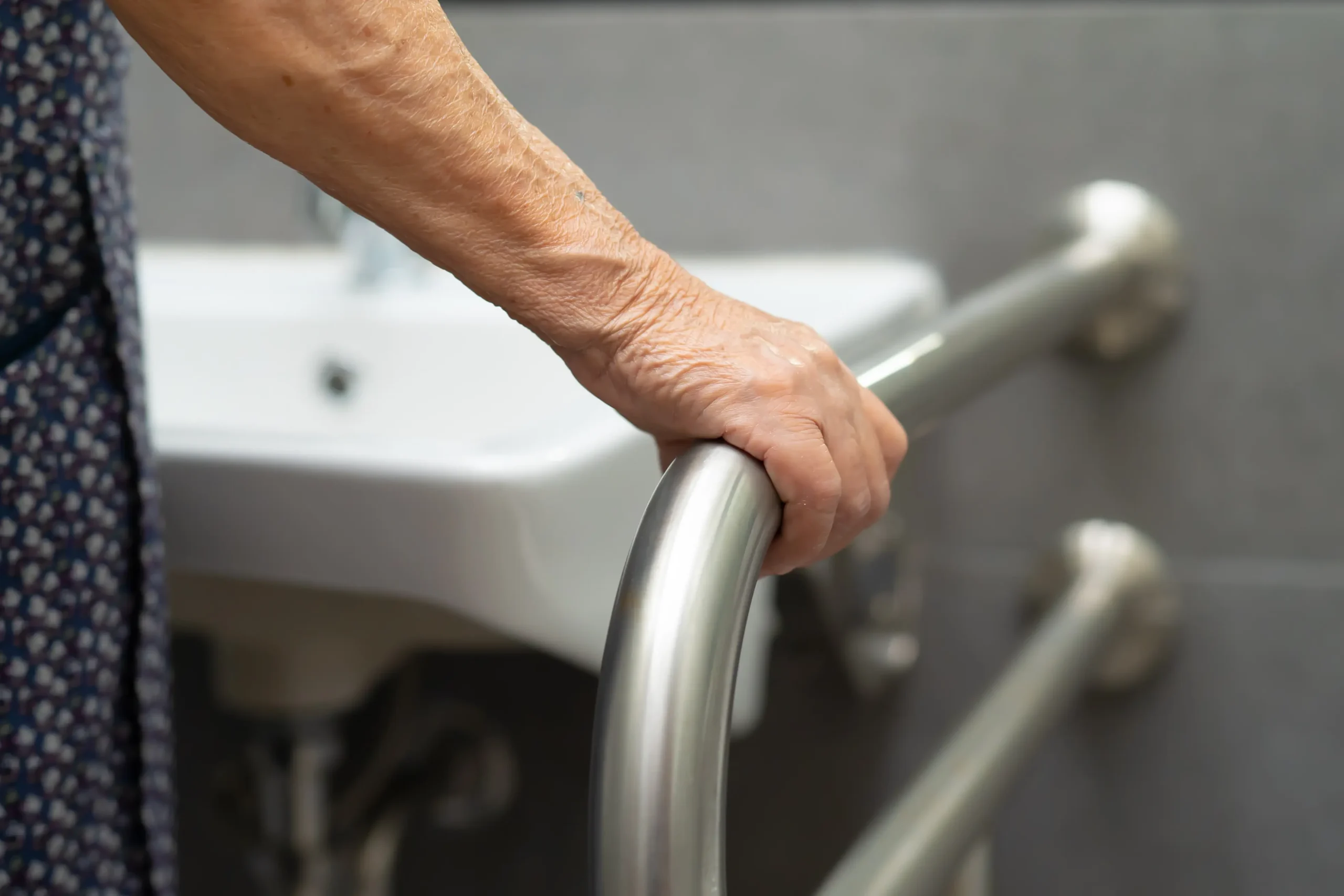Elderly hand gripping stainless steel bathroom grab bar near a sink