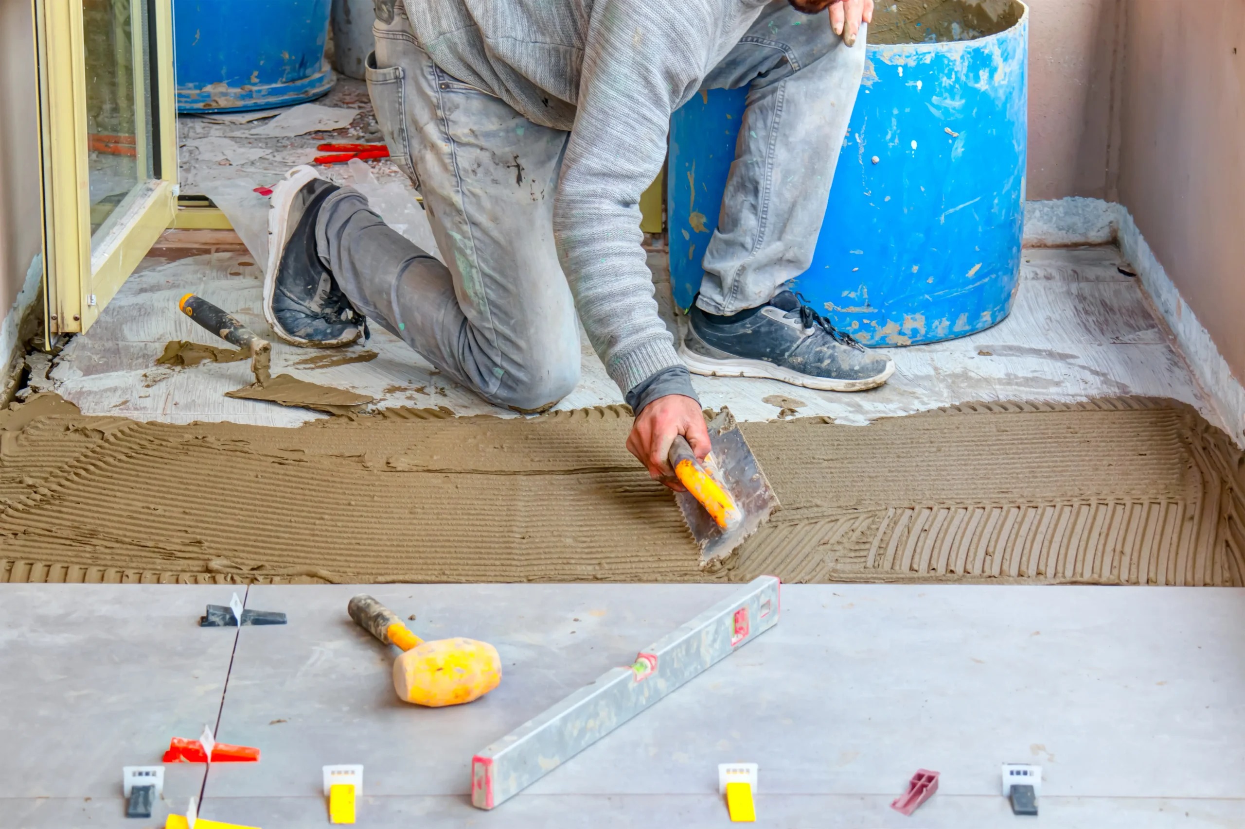 Worker spreading tile adhesive with a notched trowel during floor tile installation.