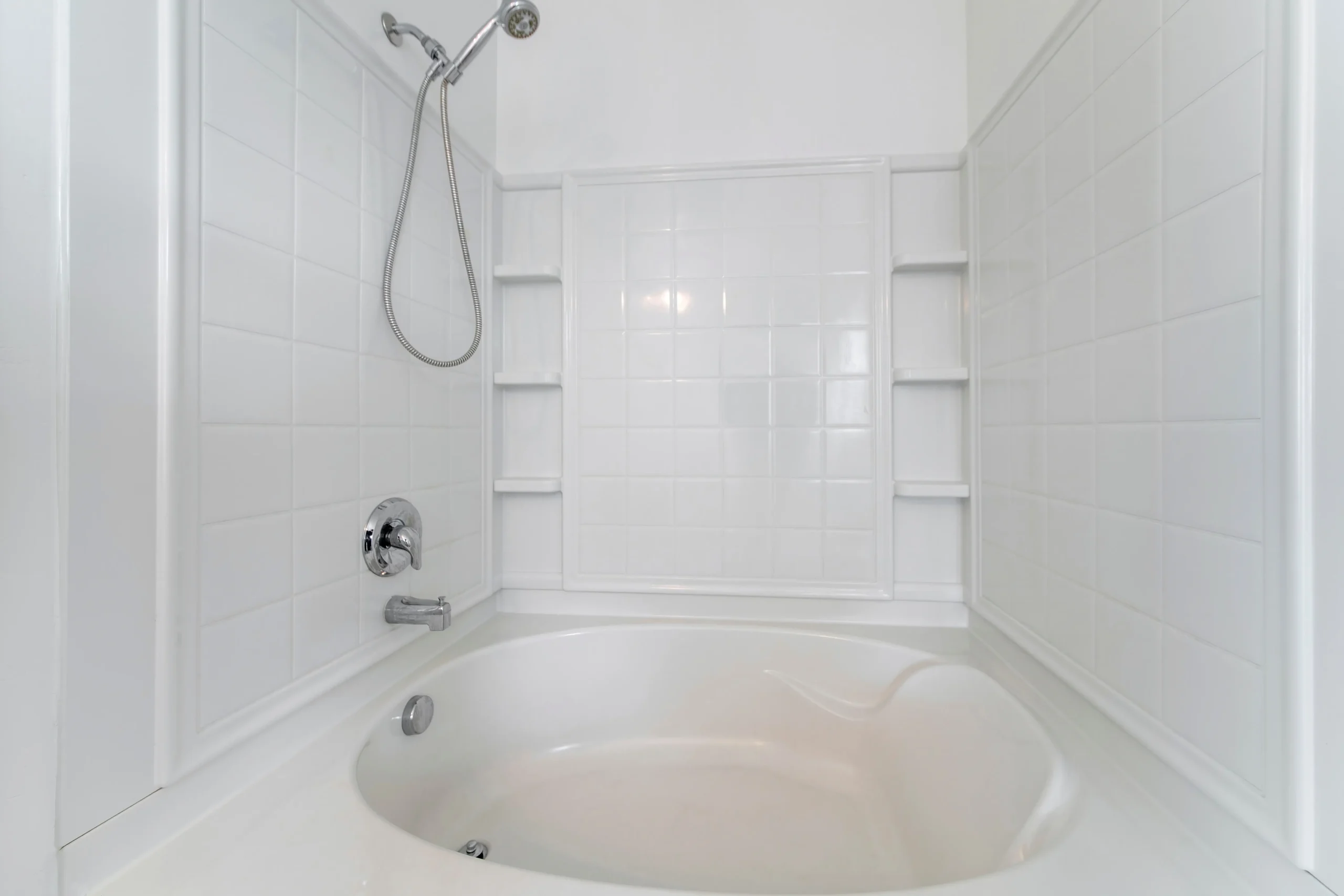 White tub and shower combo with tiled walls and built-in corner shelves
