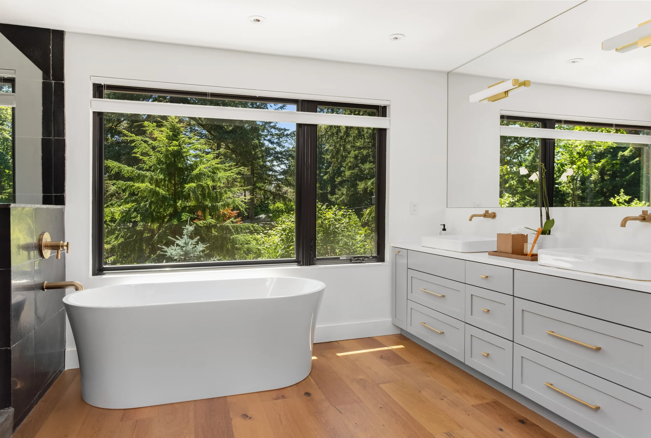 Modern bathroom with white bathtub, large window, and double vanity with gold fixtures