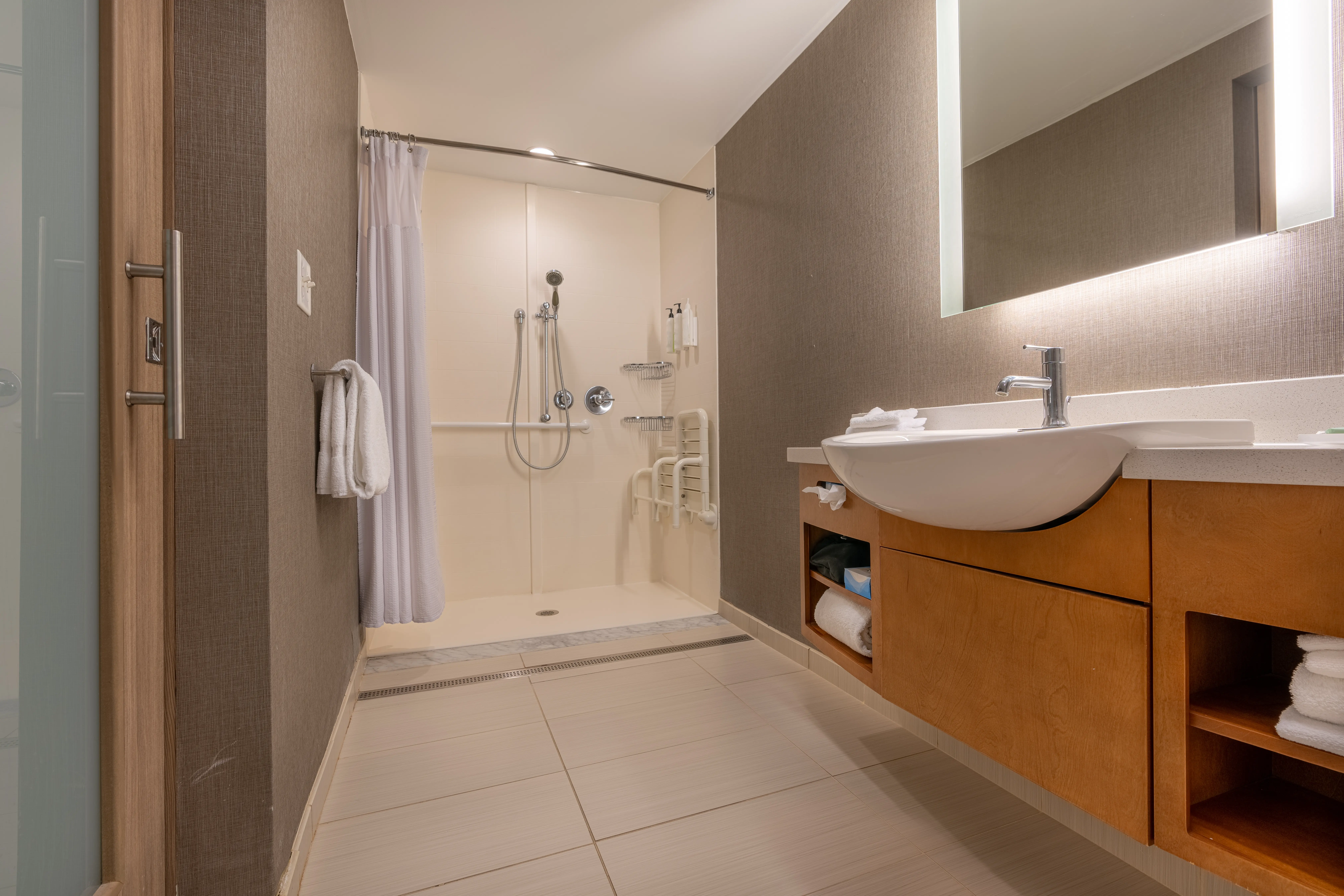 Modern accessible bathroom with roll-in shower, grab bars, folding seat, and floating vanity