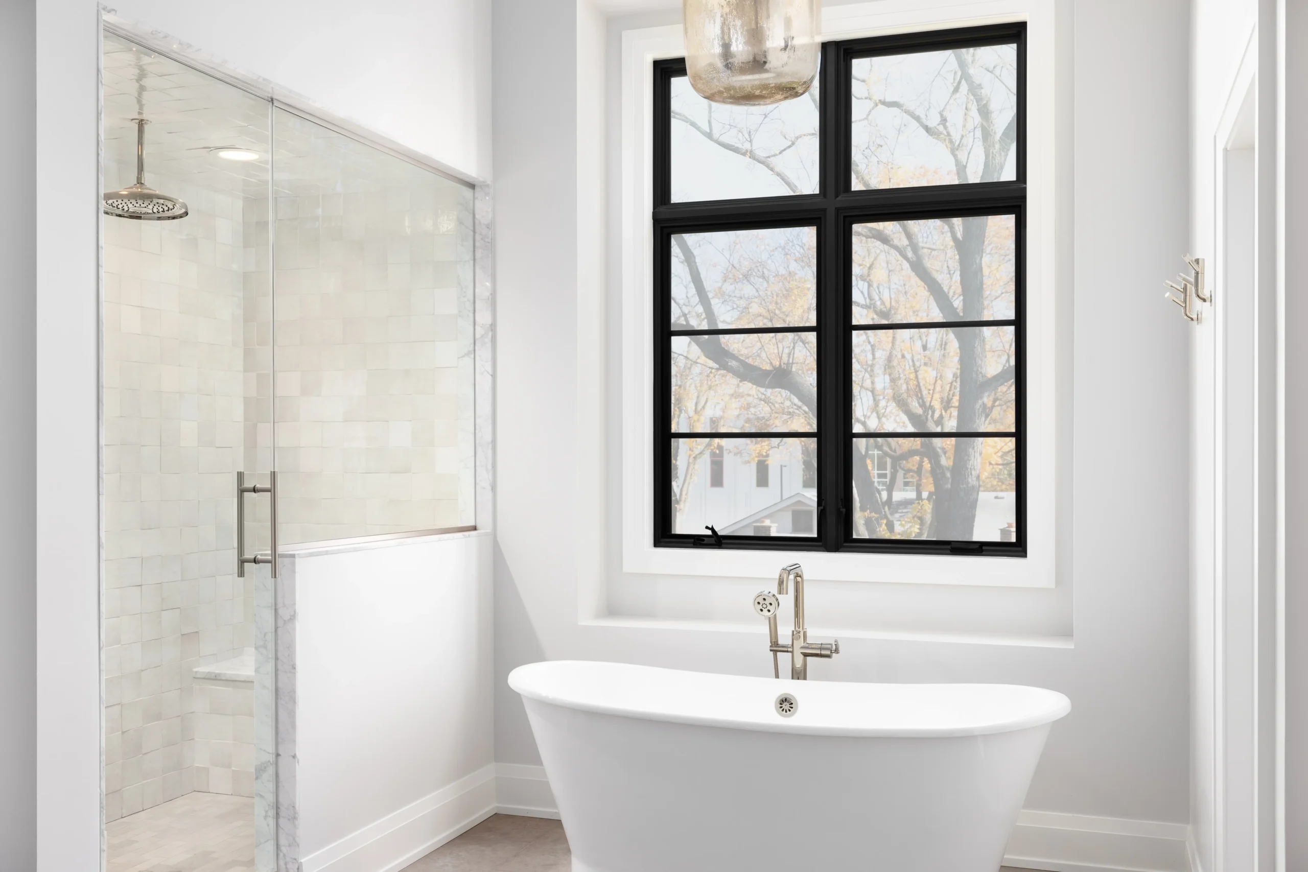 Bright bathroom with freestanding tub, large black-framed window, and glass-enclosed shower